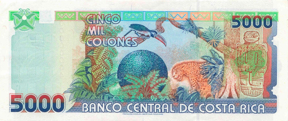 Reverse of the ₡5,000 Costa Rican banknote, featuring a tropical rainforest biodiversity scene with wildlife, lush vegetation, and elements of the country's pre-Columbian Heritage.