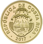Anverso de una moneda dorada de Costa Rica. En el centro se aprecia el escudo nacional en relieve, rodeado por la inscripción “REPÚBLICA DE COSTA RICA” en el borde superior. En la parte inferior figura el año 2017. La moneda presenta un acabado dorado, forma circular y detalles grabados que destacan los elementos del escudo nacional y el borde decorado.